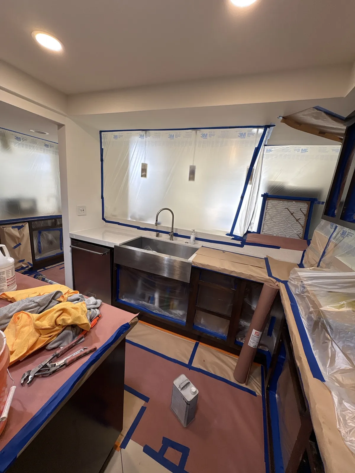 Kitchen bagged off for spraying: plastic sheeting sealed over the windows and walls, counters and floors covered, cabinet boxes masked