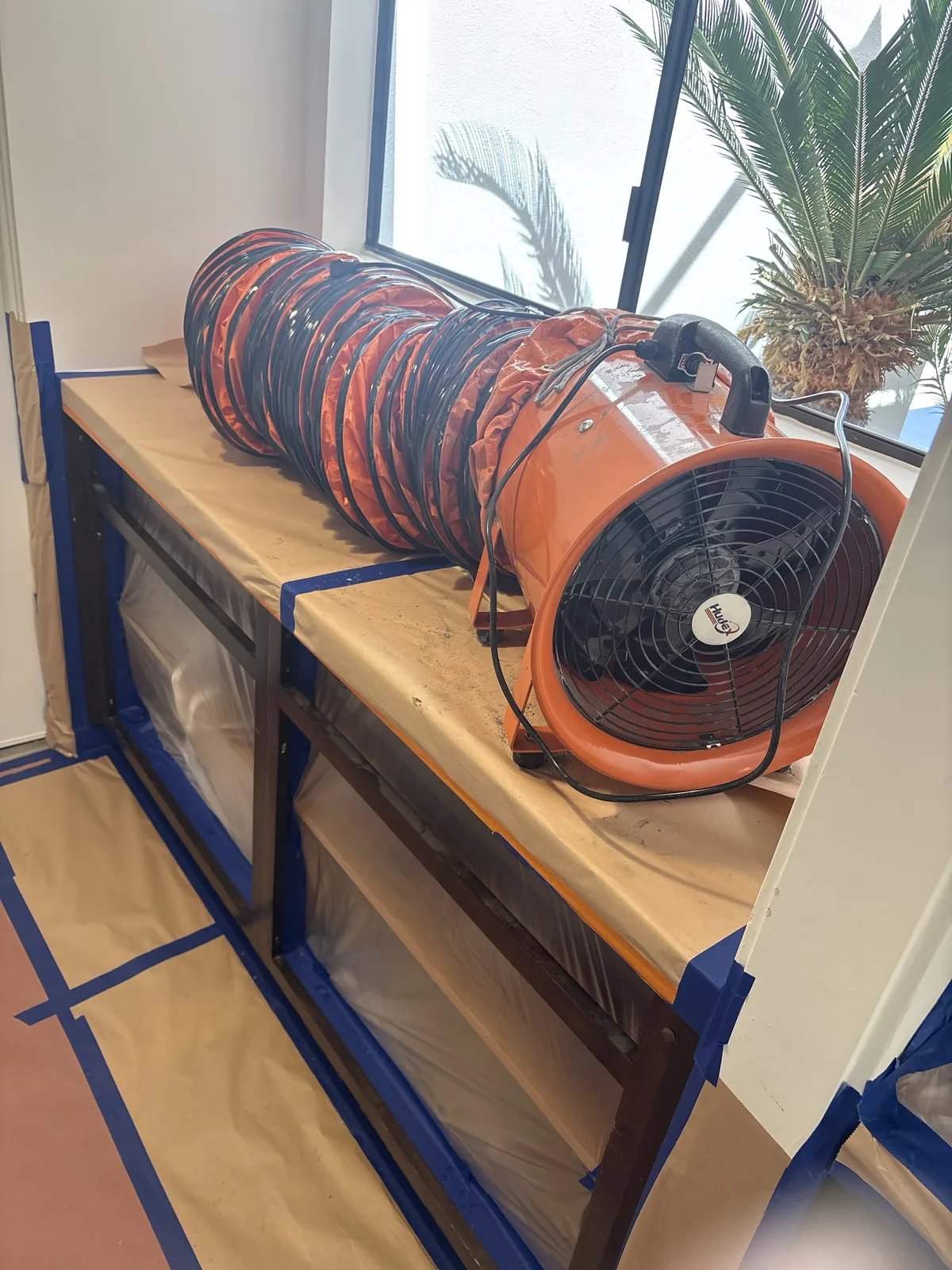 Ducted exhaust fan set up at a kitchen window to vent the sealed, negative-pressure work area outside